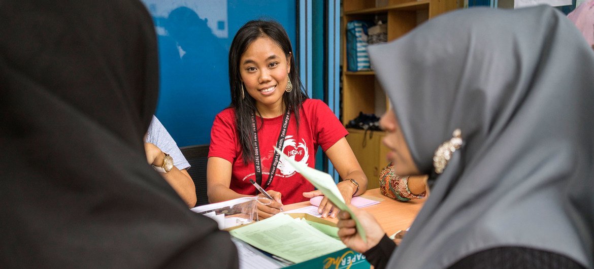Kina, a 37-year-old Indonesian domestic worker from Surabaya, Java, volunteers her time at HOME.org, an NGO in Singapore, to assist abused migrant workers. She is smiling while helping others during a consultation.