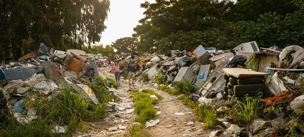 Children walk along a path through a massive e-waste dumpsite in the Felipe Cardozo neighborhood in Montevideo, Uruguay. The site is filled with discarded electronic devices and hazardous materials, highlighting global e-waste issues.