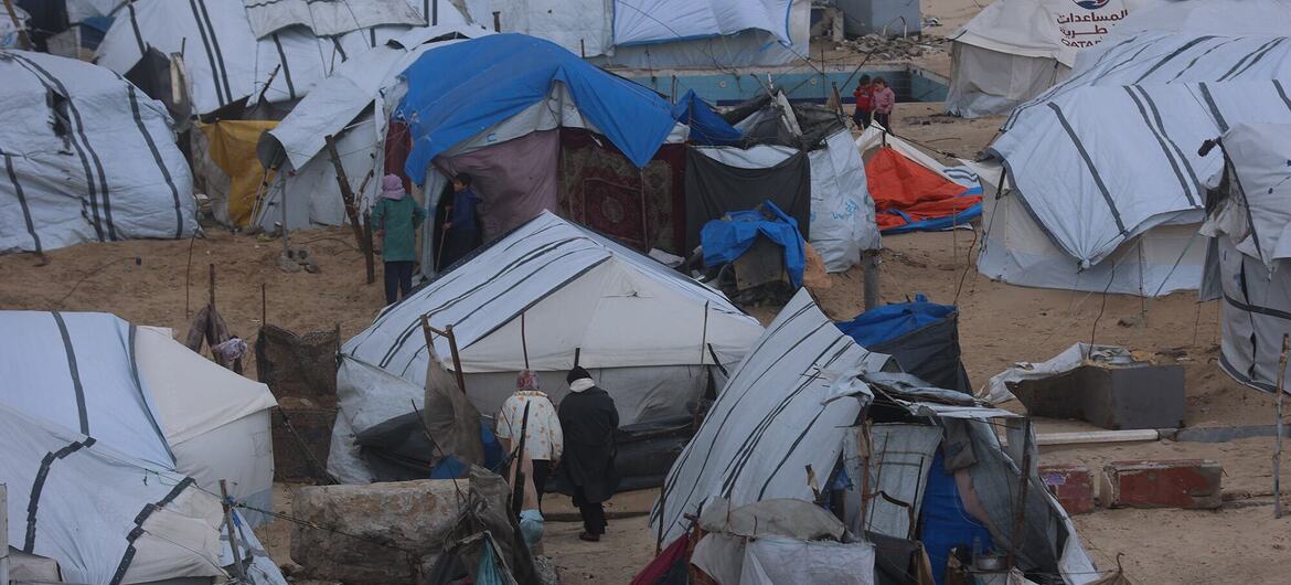 People walk through a makeshift refugee camp in Gaza, surrounded by tents and rudimentary shelters.